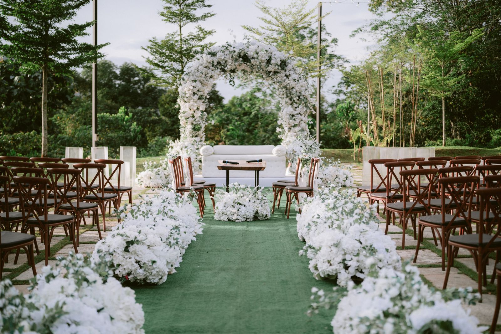 An outdoor ceremony on the lawn with a floral arch and rows of chairs