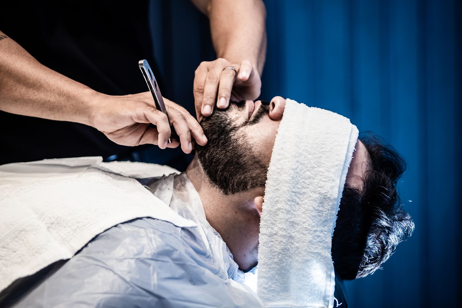 A relaxed client enjoying a hot towel and a beard trim in a reclined barber chair