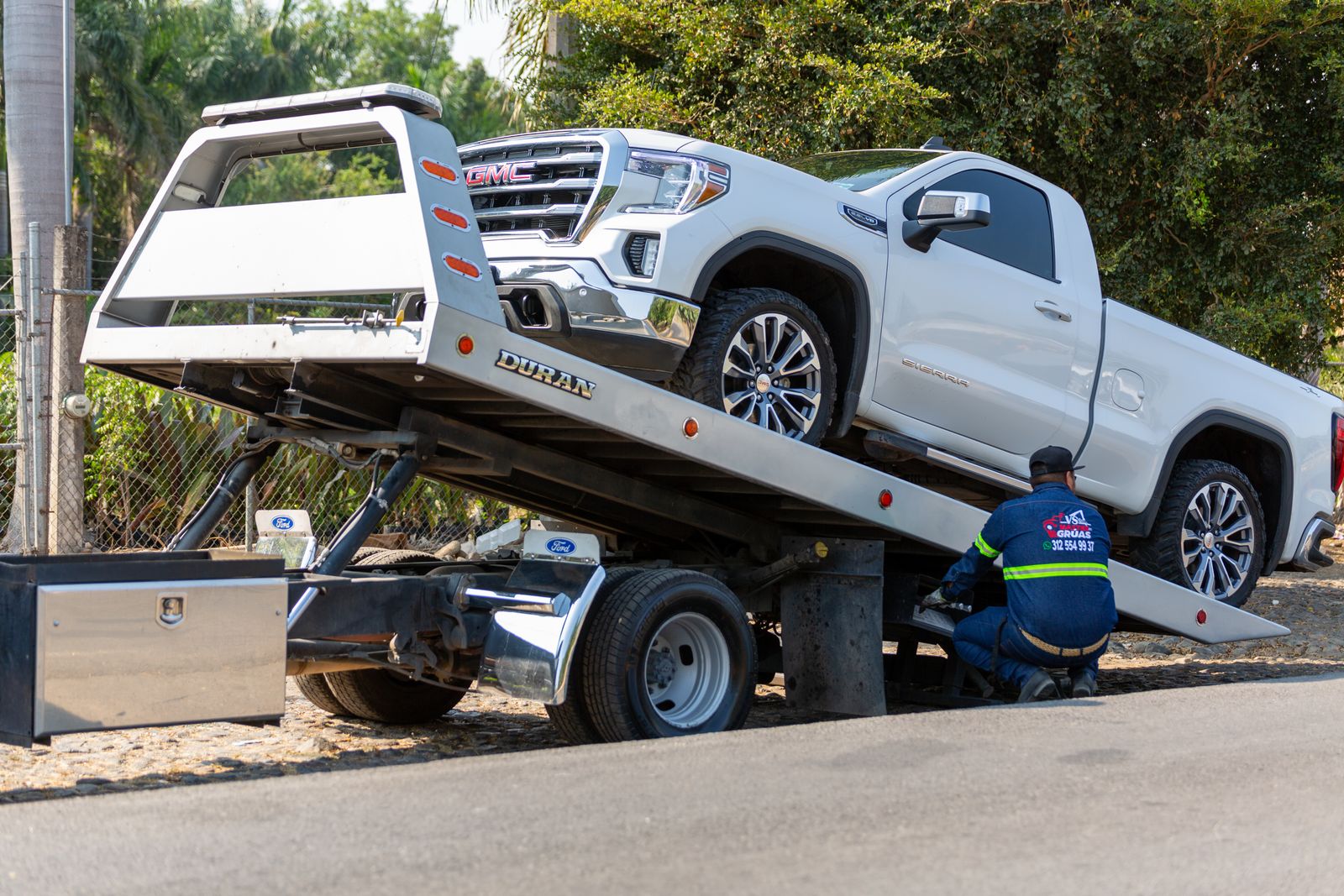 A tow truck lifting a car, with its driver standing by