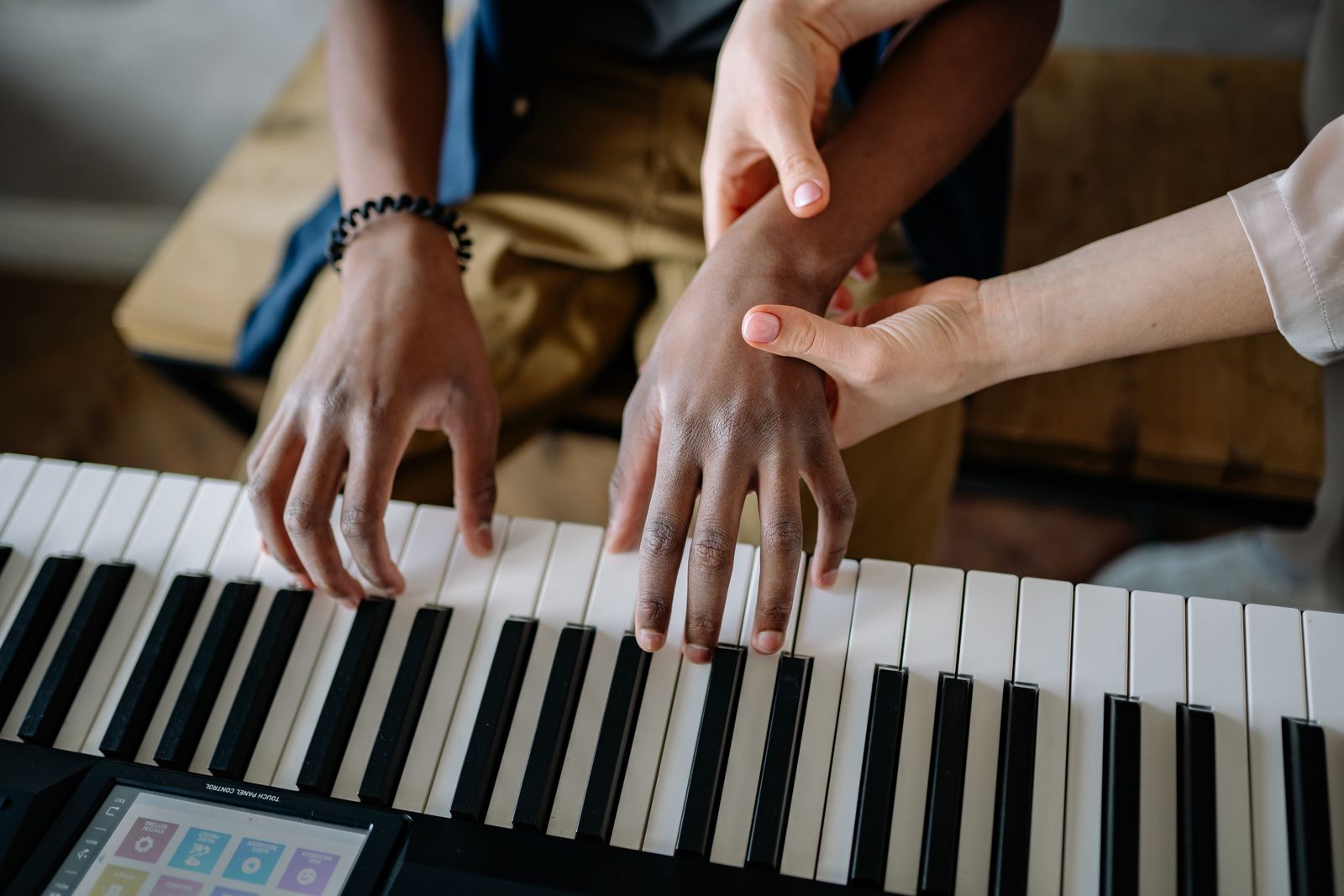A teacher sitting beside a young student at an upright piano
