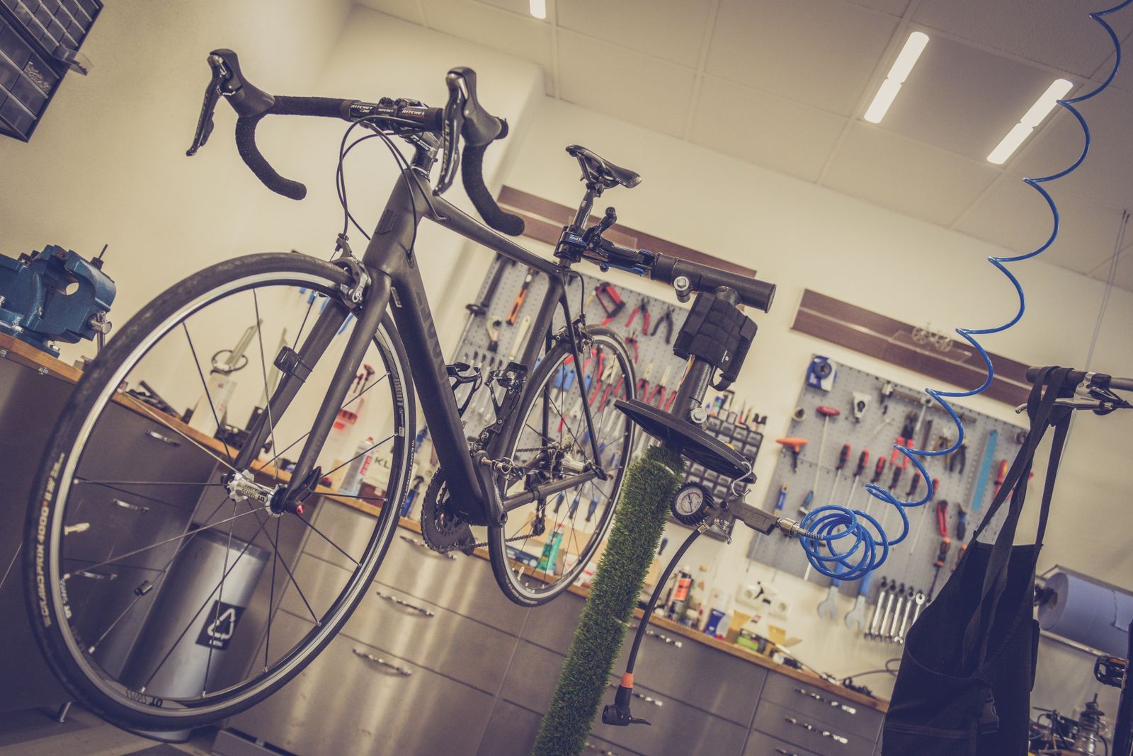 A mechanic working on a bike held in a repair stand, with tools on the wall behind