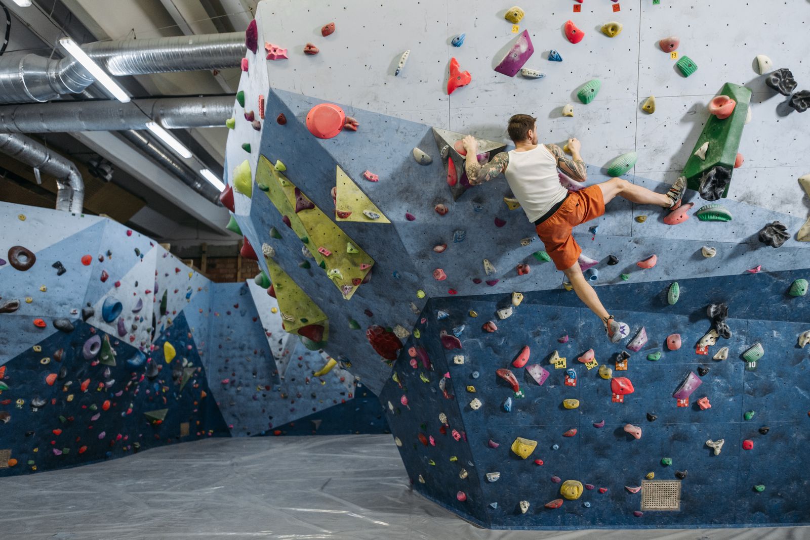 A climber reaching for a hold on a bouldering wall above thick mats