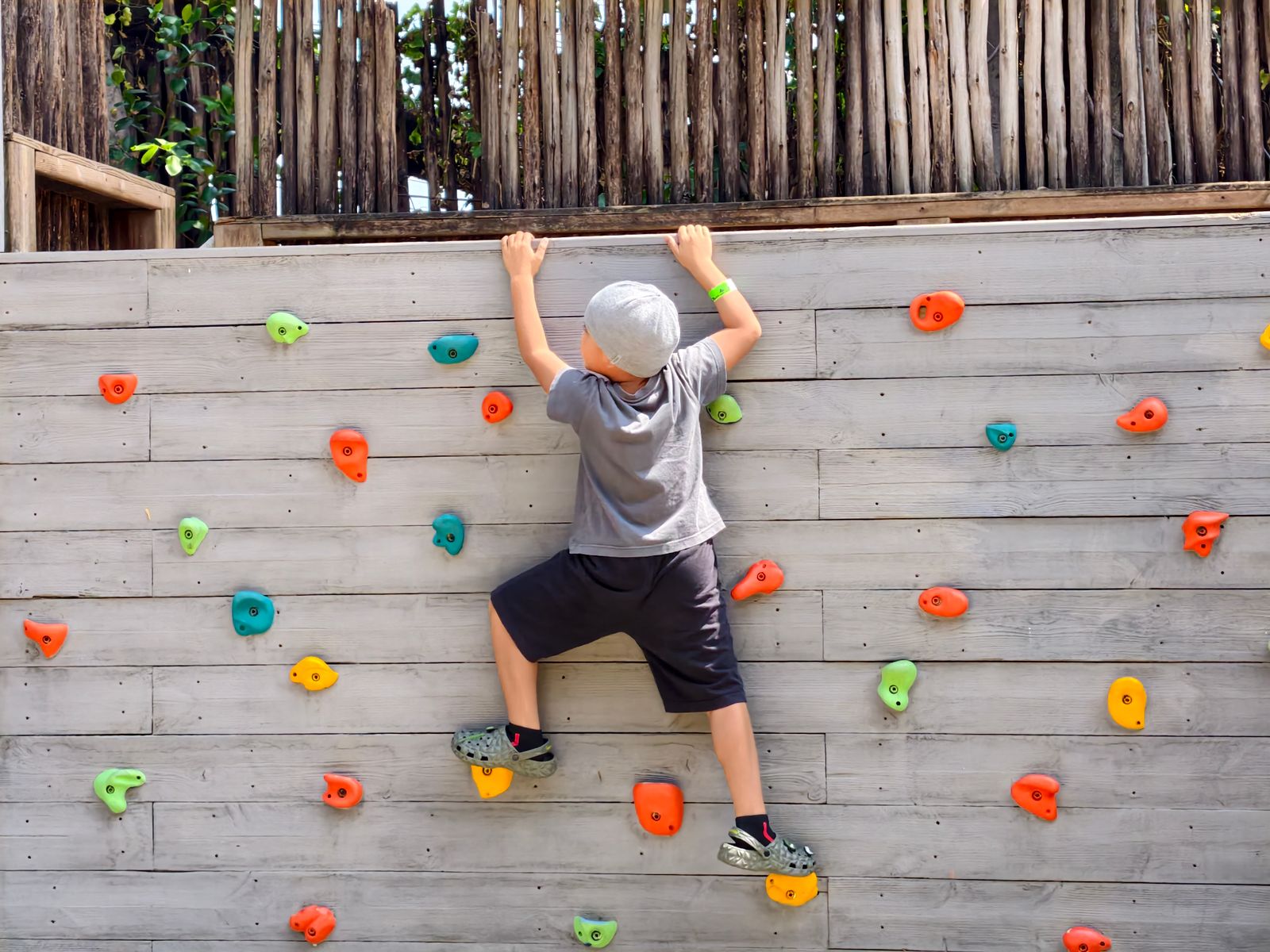 A child climbing a low wall, seen from behind, with a coach watching