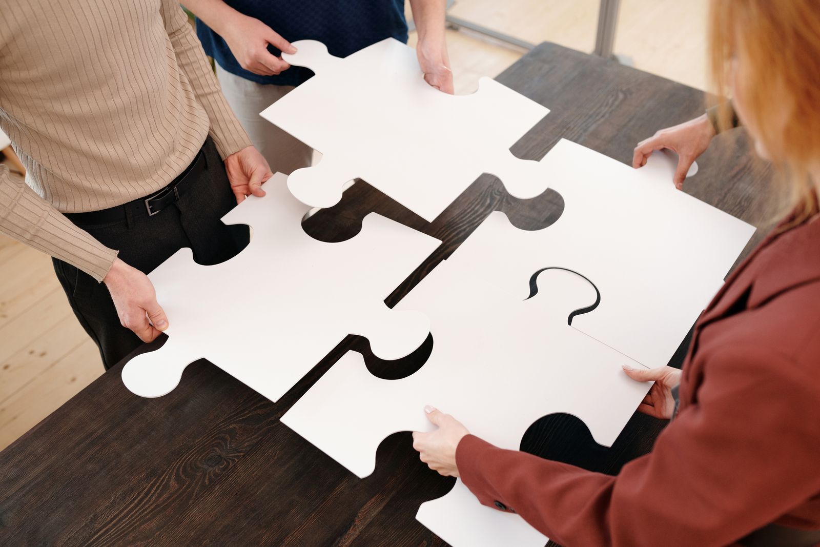 Four friends seen from behind, working together on a puzzle at a table
