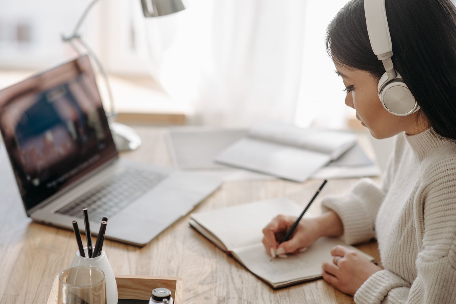 A laptop showing the teacher, headphones and a notebook on a desk